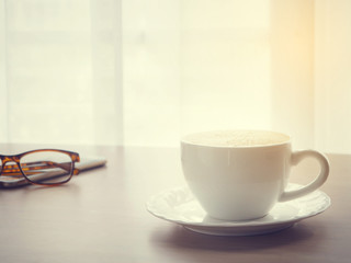 coffee cup of cappuccino with eyeglasses on smartphone, tablet, cell phone with  blurry white drape texture background, warm tone.