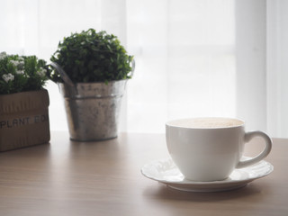 wood office table with cup of latte coffee and beautiful flower on blurry white curtain texture background.