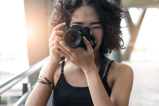 young woman using a camera to take photo outdoors at balcony building