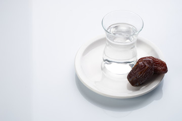 A glass of water and iftar dry dates on white saucer ready to eat for iftar time. Islamic religion and ramadan concept.  White background with copy space.