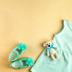 Dress and shoes for baby girl and bear toy over beige background