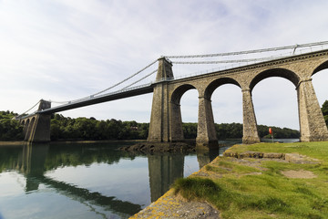 Fototapeta na wymiar Grand view of the northern-side of the historic Menai Suspension Bridge including it's reflection on the surface of the Menai Straits, Anglesey, North Wales