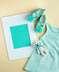 Frame, dress and shoes for baby girl over beige background with copy space