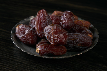 Close-up of Ramadan dates or kurma for iftar opening on silver plate on balck wooden table. Islamic religion and ramadan month concept.