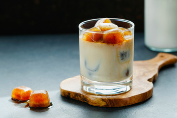Iced coffee with milk on a wooden board on a black table.