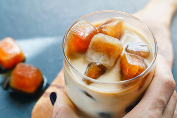 Girl holding iced coffee with milk on a wooden board on a black table. Top vew.