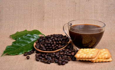 Coffee beans and wooden spoon on sack surface.