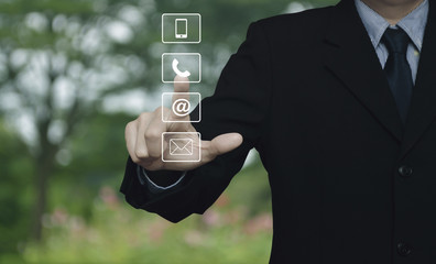 Businessman pressing telephone, mobile phone, at and email buttons over blur flower and tree in park, Customer support concept