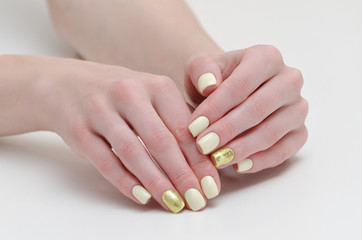 Female hands with manicure, yellow with gold covering of nails. White background.