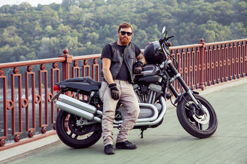 Bearded redhead biker with beard in leather jacket near bike.