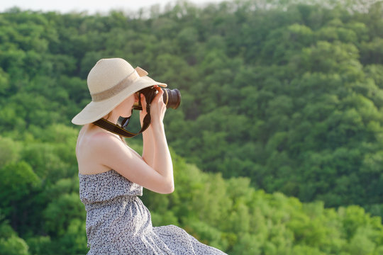 Girl in hat takes pictures against the background of green forest