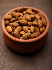 Almonds in a ceramics bowl against dark rustic wooden background