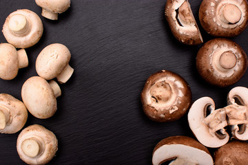 Gray and white champignons mushrooms whole and sliced lie on a stone black slate, the background