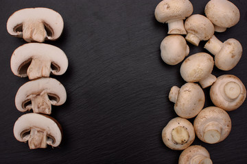 White mushrooms champignons whole and sliced lie on a stone black slate board, background