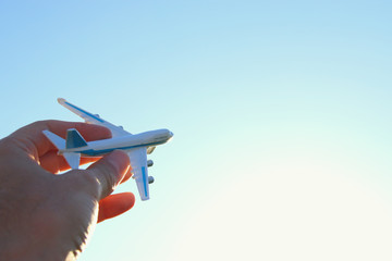 close up of man's hand holding toy airplane against blue sky