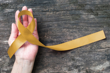 Childhood cancer awareness with gold ribbon symbolic color on helping hand on old aged wood
