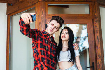 Fototapeta na wymiar Happy romantic couple taking a photo with smart phone. Beautiful young girl and man hug and laugh taking a selfie. Urban fashion style