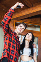 Happy romantic couple taking a photo with smart phone. Beautiful young girl and man hug and laugh taking a selfie. Urban fashion style