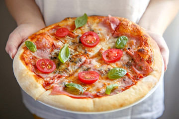 Pizza. Woman holding fresh Italian margherita with salami, basil and tomato.