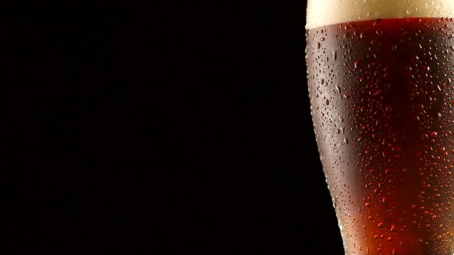 Dark beer closeup. Pint of cold craft beer isolated on black background. Rotation 360 degrees. 4K UHD video 3840x2160