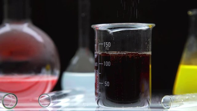 Different types of chemical laboratory glassware with liquids inside: a subject video recording on a black background. Round bulb, beaker and test tube. Color experiments.