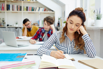 Young student making notes while reading book