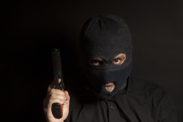 criminal bandit man wearing in balaclava holds a gun in his hand on black background
