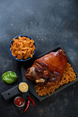 Whole baked pork knuckle and braised cabbage on a dark metal background, high angle view with space