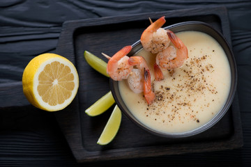 Potato and shrimps cream-soup on a black wooden serving tray, above view, studio shot