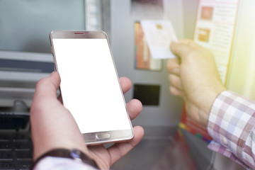 Hand of a man with a credit card, using an ATM. Man using an atm machine with his credit card. Closeup of male hands using smart phone while typing on ATM.
