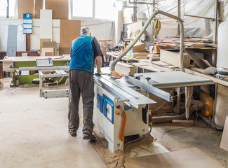 Worker sawing wood panel saw machine for furniture factory. Circular saw.