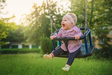 Shifting the little baby girl on swings on a summer evening. - obrazy, fototapety, plakaty