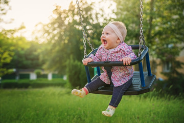 Shifting the little baby girl on swings on a summer evening.