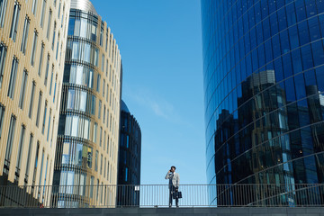 Fototapeta premium Modern trader calling against blue sky between skyscrapers