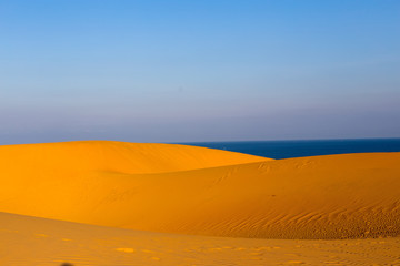 Fototapeta na wymiar Yellow sandy wavy dunes with blue sea at background