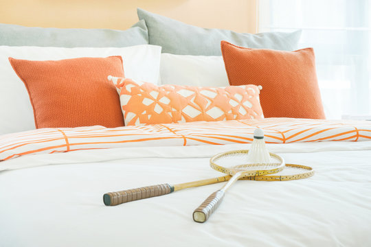 Modern bedroom interior with orange and gray pillows with rackets and shuttlecock on bed