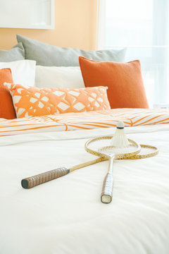Orange color scheme bedding with rackets and shuttlecock on bed at home