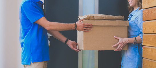 Smiling delivery man in blue uniform delivering parcel box to recipient - courier service concept