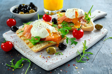 Poached egg on grilled toast with smoked salmon, rucola, olives, vegetables and orange juice. on white board. healthy breakfast