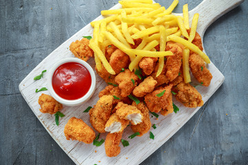 Fried crispy chicken nuggets with french fries and ketchup on white board