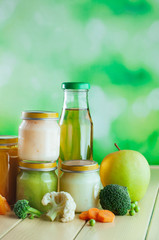 Fototapeta na wymiar Jars with vegetable and fruit puree and juice near apples, broccoli, cauliflower, pea and carrot