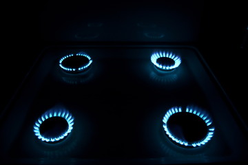 four burning gas stove hob blue flames close up in the dark on a black background angle