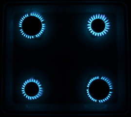 four burning gas stove hob blue flames close up in the dark on a black background top view