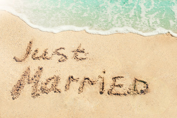 Text JUST MARRIED written on sand near water. Honeymoon concept