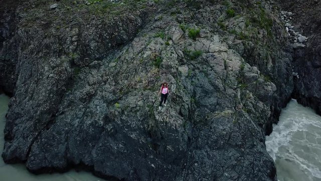 Aerial. woman traveler with backpack enjoying a stunning view standing on the edge of the cliff on a mountain river. Altai, Siberia. Aerial camera shot