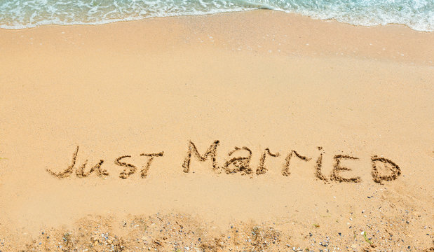 Text JUST MARRIED written on sand near water. Honeymoon concept