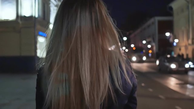 A blonde girl is walking around the night city. Shooting from behind and hair close up