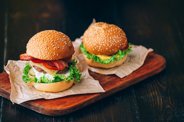 Bright juicy appetizing burgers with a cutlet, cheese, marinated cucumbers, tomatoes and bacon in the hands of a girl, a girl in special gloves for burgers