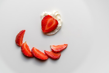 A top view of sliced strawberries and cream on a white plate. Pieces of berries are nicely laid out on a plate.