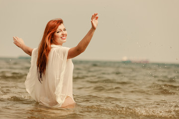 Fototapeta na wymiar Redhead woman playing in water during summertime